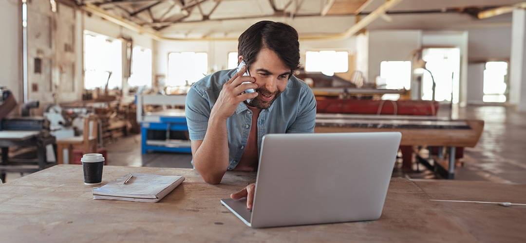 Carpenter using laptop and cell phone at work shop