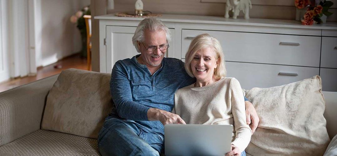 Couple sitting on couch smiling at laptop